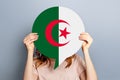 Female hands holding a round information poster with Algeria flag isolated over grey studio background