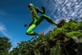 alien athlete in mid-jump, with vibrant green foliage and sky in the background