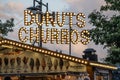Donuts and churros sign at a food truck at night..