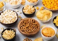 All classic potato snacks with peanuts, popcorn and onion rings and salted pretzels in bowl plates on light background. Twirls