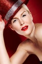 All that glitters. Portrait of a beautiful showgirl with red lipstick and a sparkly red hat against a red background.