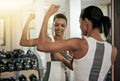 All her hard work has paid off. A young woman flexing her muscles in front of the mirror at the gym.