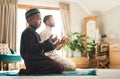 We all need a prayer circle. a young muslim man and his son praying in the lounge at home.