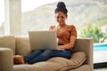 All these status updates on social media is too funny. Shot of a beautiful young woman sitting on a sofa using a laptop Royalty Free Stock Photo