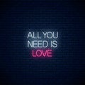 All you need is love - glowing neon inscription phrase on dark brick wall background. Motivation quote in neon style Royalty Free Stock Photo