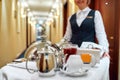 All that you need. Waitress in uniform delivering tray with food in a room of hotel. Room service. Focus on tableware