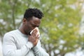 Allergic black man blowing on wipe in a park on spring season