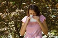 Allergy concept. Sneezing young girl with nose wiper among blooming trees in park Royalty Free Stock Photo