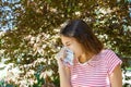 Allergy concept. Sneezing young girl with nose wiper among blooming trees in park Royalty Free Stock Photo