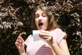 Allergy concept. Sneezing young girl with nose wiper among blooming trees in park Royalty Free Stock Photo