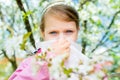 Allergy. Little girl is blowing her nose near spring tree in bloom - sneezing girl. Child with a handkerchief Royalty Free Stock Photo