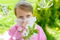 Allergy. Little girl is blowing her nose near spring tree in bloom - sneezing girl. Child with a handkerchief Royalty Free Stock Photo