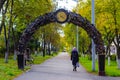 Alley with lanterns and a bench under an iron arch with a clock. Beautiful cityscape of alley with autumn trees. Royalty Free Stock Photo