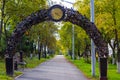 Alley with lanterns and a bench under an iron arch with a clock. Beautiful cityscape of alley with autumn trees. Royalty Free Stock Photo