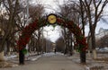 Alley with lanterns and benches under an iron arch decorated with red roses with a clock. Spring city beautiful landscape Royalty Free Stock Photo