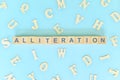 Alliteration figure of speech concept in English grammar class lesson. Wooden blocks typography flat lay in blue background. Royalty Free Stock Photo