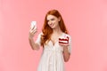 Alluring caucasian birthday girl with red long hair in white dress, taking selfie to post internet social media during b