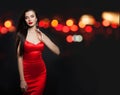 Alluring woman in red silky dress and black carnival mask on background with abstract night glitter bokeh Royalty Free Stock Photo