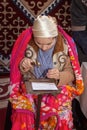 Girl in national dress works a strip of metal for a bracelet with a hammer against the