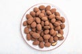 Almond in chocolate dragees on ceramic plate on white concrete background. Top view, close up Royalty Free Stock Photo