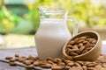 Almond milk in glass pitcher and almond nuts in wooden bowl