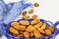 Almond nuts lie in an oval-shaped blue glass bowl and on a white surface, close-up Royalty Free Stock Photo