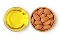 Almond oil in glass bowl and almonds in wooden bowl on white background