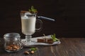 Almond vegetable milk in an Irish glass with a cinnamon and a honey spoon, nuts in a glass jar, on a dark background