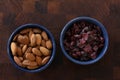 Almonds and cranberrys lying in blue bpowls on dark wooden background. Top view image