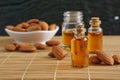 Almonds oil in transparent glass bottles and pile of roasted almonds on brown wooden mat, copy space concept.