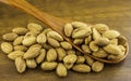 Almonds seeds pour from wood spoon on textured wooden background, top view.