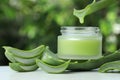 Aloe vera juice dripping from leaf into jar with cream on white table against green blurred background, closeup Royalty Free Stock Photo