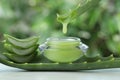 Aloe vera juice dripping from leaf into jar with cream on white table against green blurred background, closeup Royalty Free Stock Photo