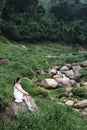 Alone Asian woman wear white dress is sitting on the rock in forest. Freedom in the nature.