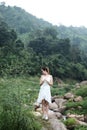 Alone Asian woman wear white dress is standing on the rock in forest. Freedom in the nature.