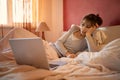 Alone bored woman in pajamas chilling at home, lying on bed and watching laptop computer. Royalty Free Stock Photo