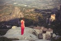 Alone girl in a red dress on the edge of the rock and prays at the monasteries of Meteora. Female on the rock and m