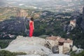 Alone girl in a red dress on the edge of the rock and prays at the monasteries of Meteora. Female on the rock and m