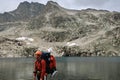 Alone hiker man with backpack and helmet is staying by the mountain lake. Extreme backpacker tourist in wild nature