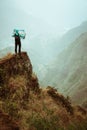 Alone hiker with map of the island staying on a rocky ledge in front of a gorgeous panorama view of high mountain ranges Royalty Free Stock Photo