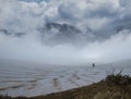 Alone hiker walk through snowbound mountain valley in dense mist