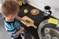 Alone independence vegetarian child cuts green cucumber with knife in kitchen, vegan kid montessori training, side view Royalty Free Stock Photo