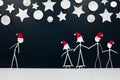 Alone man beside a complete family stick figure wearing santa hat in black background with stars and silver christmas ornaments.