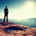 Alone man in red cap on peak of sharp peak in rock empires park and watching over the misty and foggy morning valley to Sun. Beaut Royalty Free Stock Photo