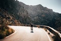 Alone man on road bicycle ride up-hill in big mountains. Orange sunset light in background