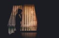 Alone man silhouette standing with hand on chin at the window closed with curtains in darkroom. Man stands at window alone, Royalty Free Stock Photo