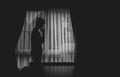 Alone man silhouette standing with hand on chin at the window closed with curtains in darkroom. Man stands at window alone, Royalty Free Stock Photo