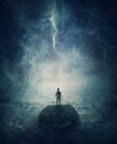 Alone man stands on a small rock island, lost in the middle of the ocean under the stormy night sky. Failure and despair concept,