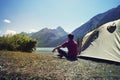 Alone man travel near the lake mountain background, travel alone concept. Young tourist guy sitting after a green tent and looking Royalty Free Stock Photo