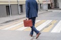 Alone middle-aged gray-haired businessman in a blue suit with briefcase laughing while calling by phone walks on the crosswalk on Royalty Free Stock Photo